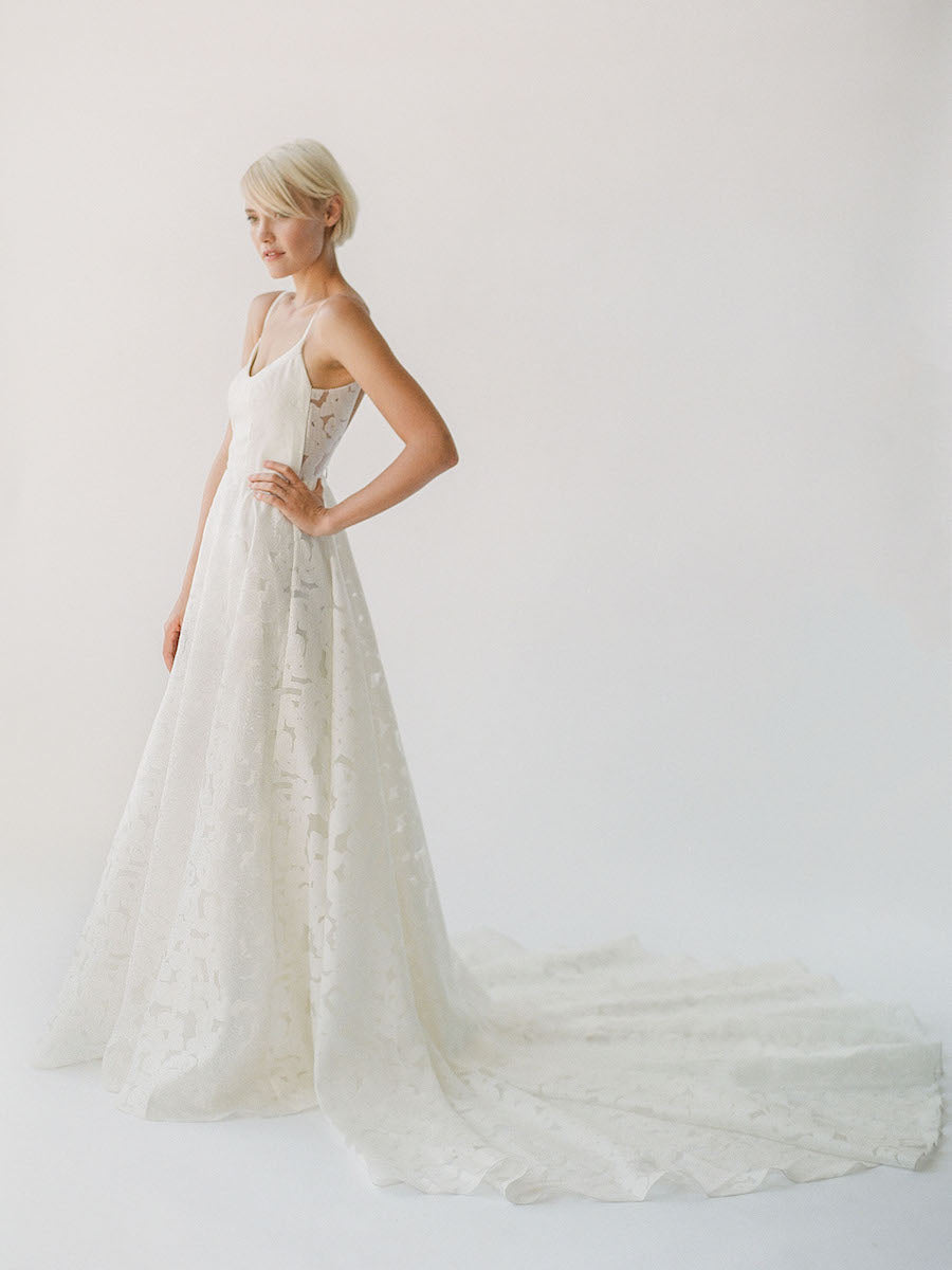 Simple and effortless wedding gown with sheer floral lace, a long train, and a low scoop back