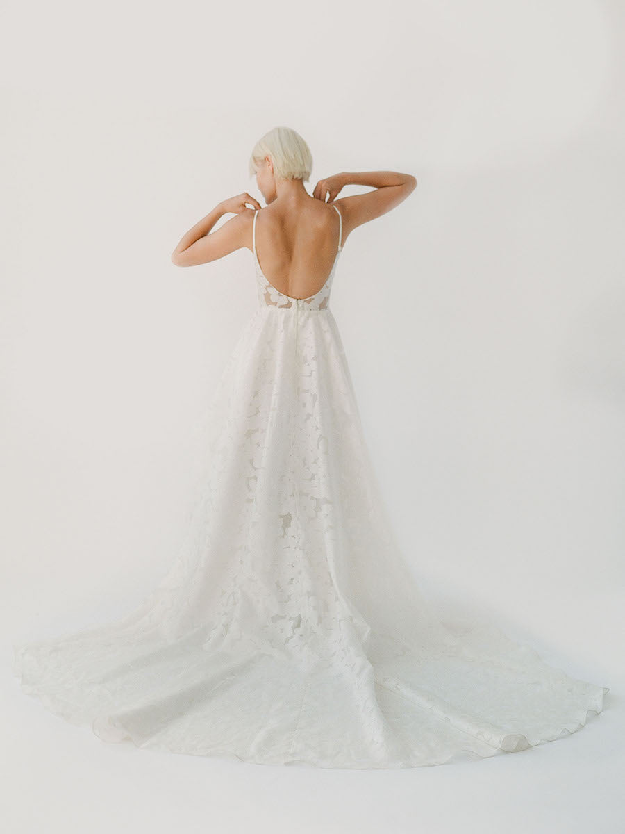 Simple and effortless wedding gown with sheer floral lace, a long train, and a low scoop back